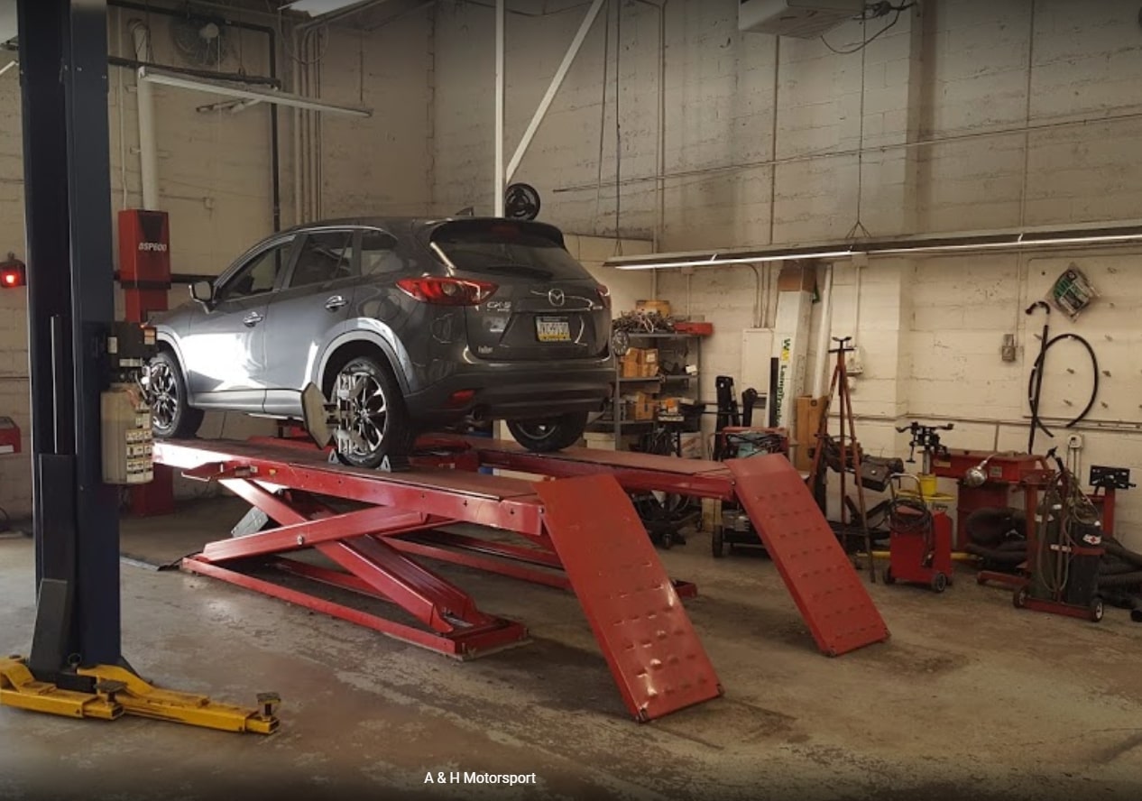 A car undergoing maintenance inside a garage, surrounded by tools and equipment, indicating regular care and upkeep